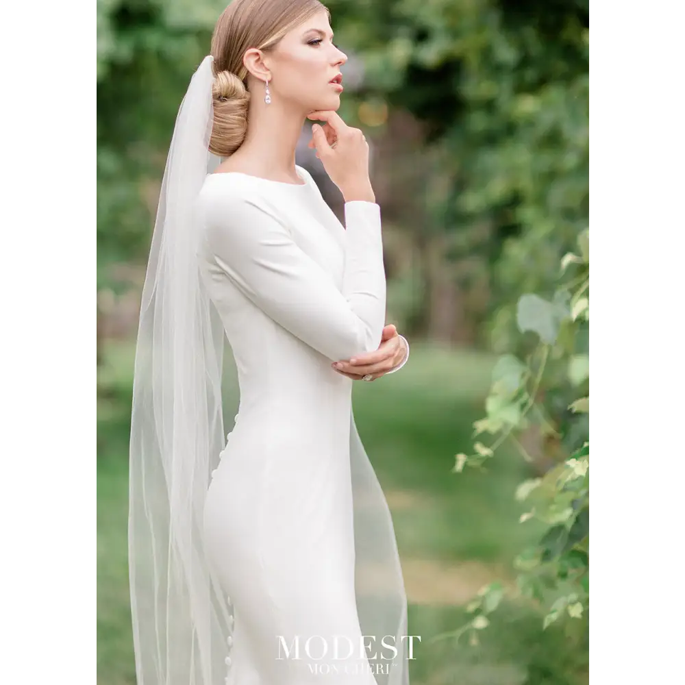 Your own royal moment in this simple and elegant stretch jersey trumpet gown featuring long sleeves, a bateau neckline, a dropped waist, princess seams, a zipper back with covered buttons down to the hem and a chapel train.#utahbridalshop #weddingdresses #weddingaccessories #bridalcloset #classyweddings #brides #utahweddings #designerweddinggowns #modestgowns #trendyweddingdresses #uniqueweddinggowns 